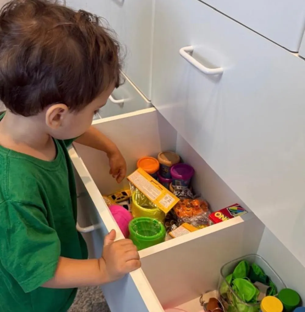 Criança escolhendo um brinde na gaveta de surpresas, cheia de brinquedos coloridos